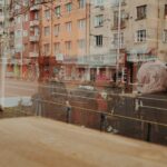 ガラス窓に重なって映る街の建物。経験と感覚情報が重なる知覚のイメージ