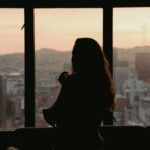 窓から街を見つめる人物。理想の未来と現状を考えるイメージ